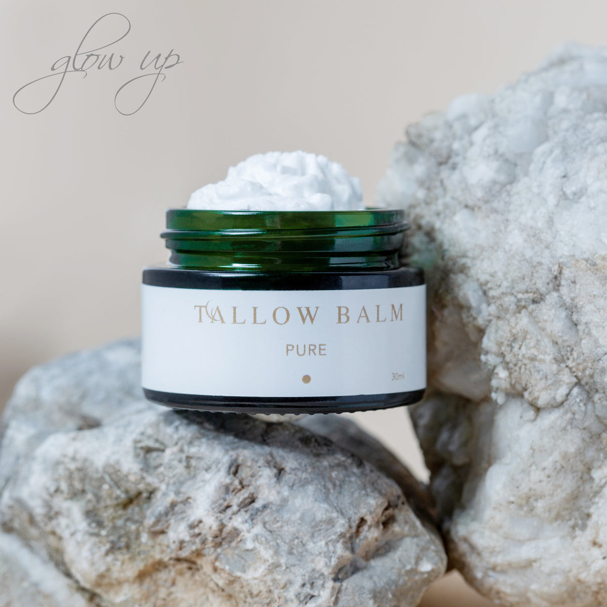 Swiss Tallow Balm Pure im grünen Glastiegel auf weißen Natursteinen mit cremiger Textur und „glow up“ Schriftzug im Hintergrund