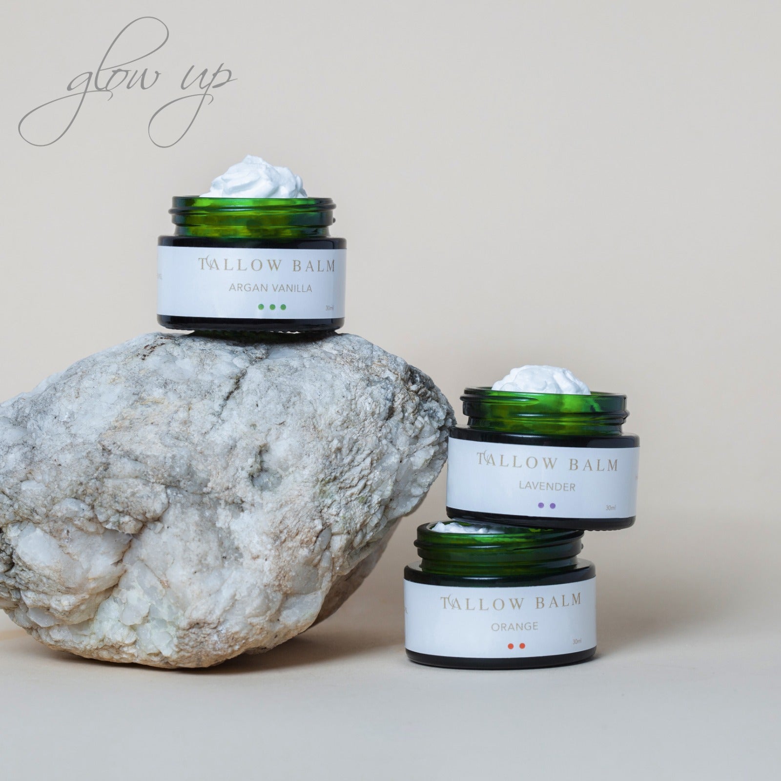 Drei geöffnete Swiss Tallow Balms in den Sorten Argan Vanilla, Lavender und Orange, stilvoll arrangiert auf Naturstein vor beigem Hintergrund