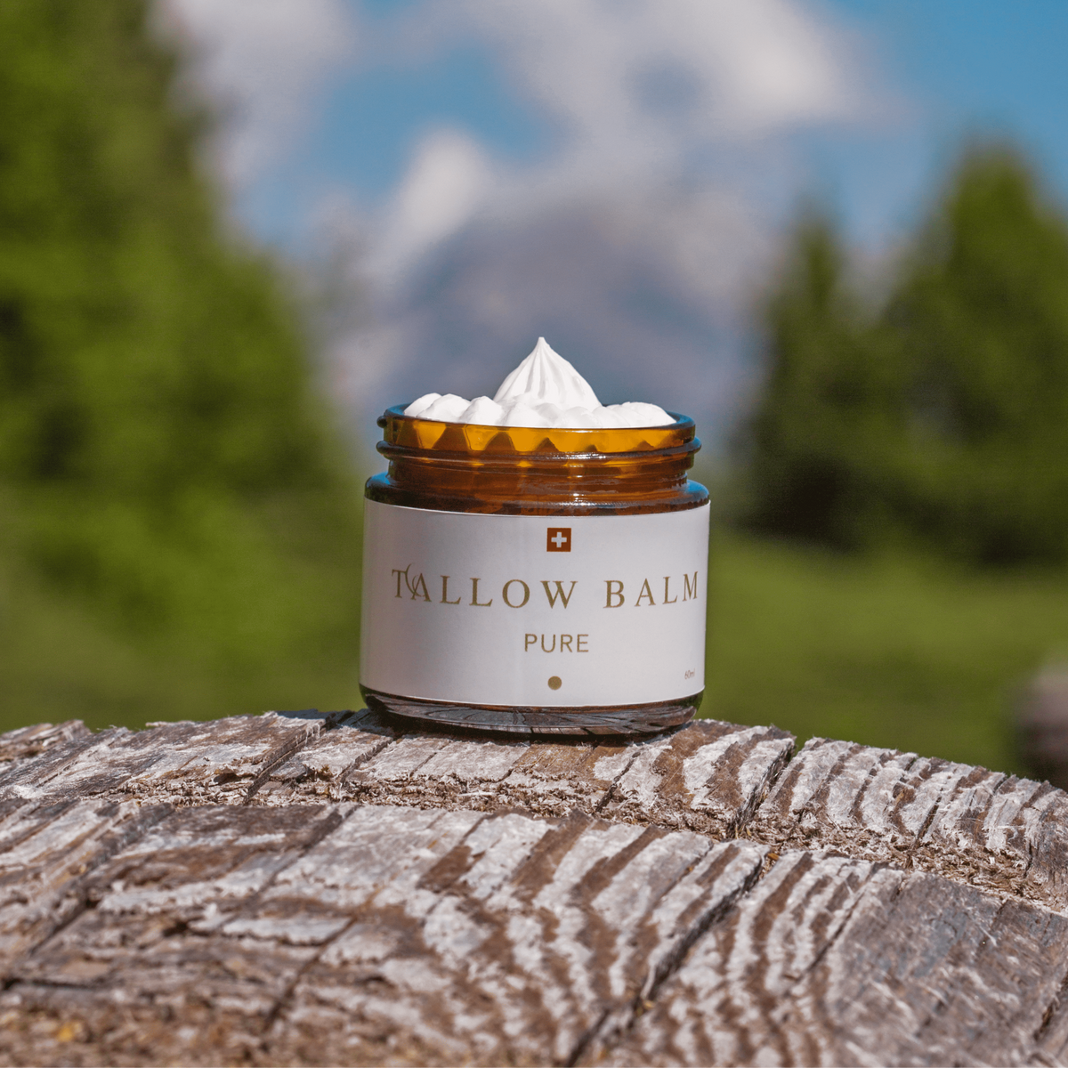 Swiss Tallow Balm Pure auf rustikalem Holz im Alpenpanorama, mit cremiger Textur und grüner Natur im Hintergrund