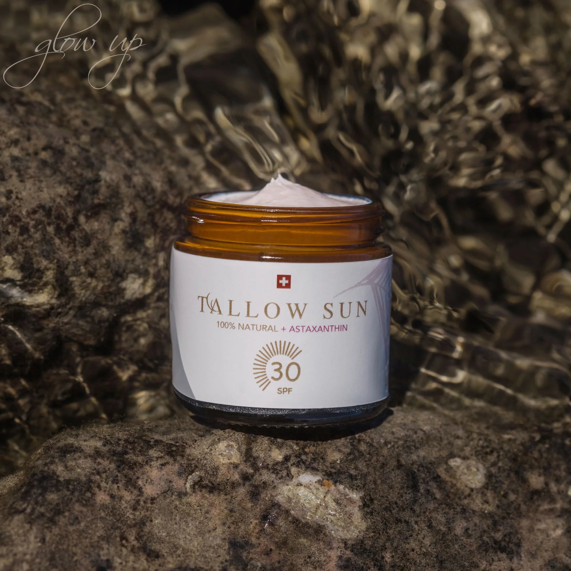 Jar of Swiss Tallow Sun sunscreen with SPF 30 and astaxanthin on a rock, with sparkling water and sun reflections in the background