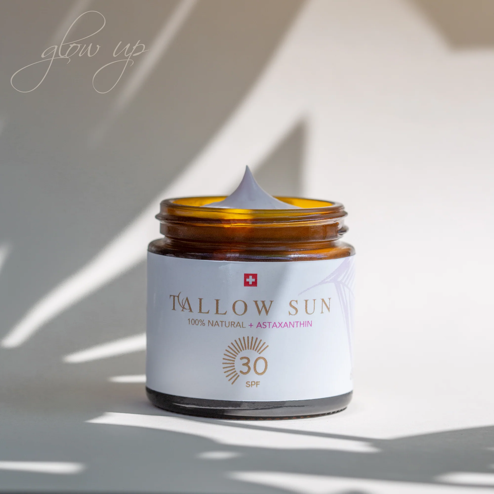 Tiegel der Swiss Tallow Sun Sonnencreme mit SPF 30 unter Lichtspiel aus Schatten und Sonnenstrahlen auf hellem Hintergrund