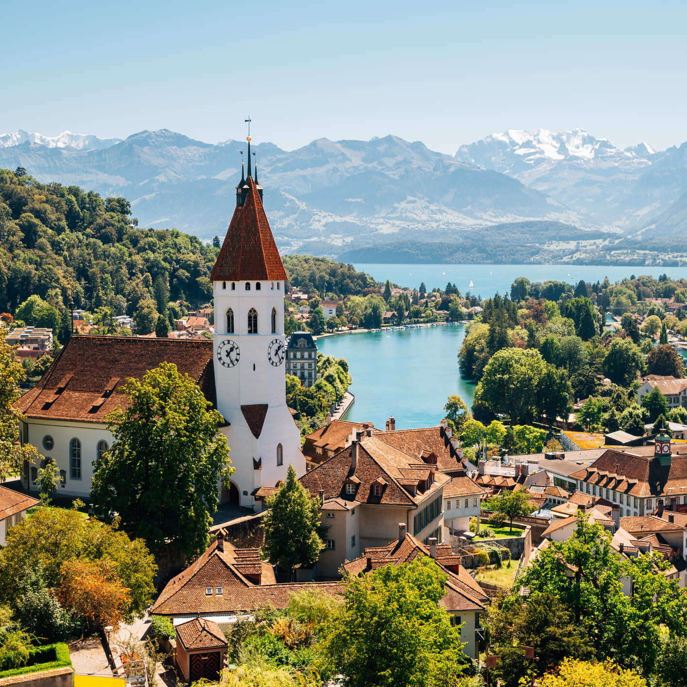 Blick über die Altstadt von Thun mit Schlosskirche, Aare und Alpenpanorama im Hintergrund an einem sonnigen Tag